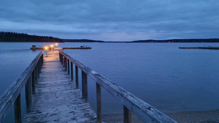 Träbrygga med små lampor ut mot havet i blå skymning.
